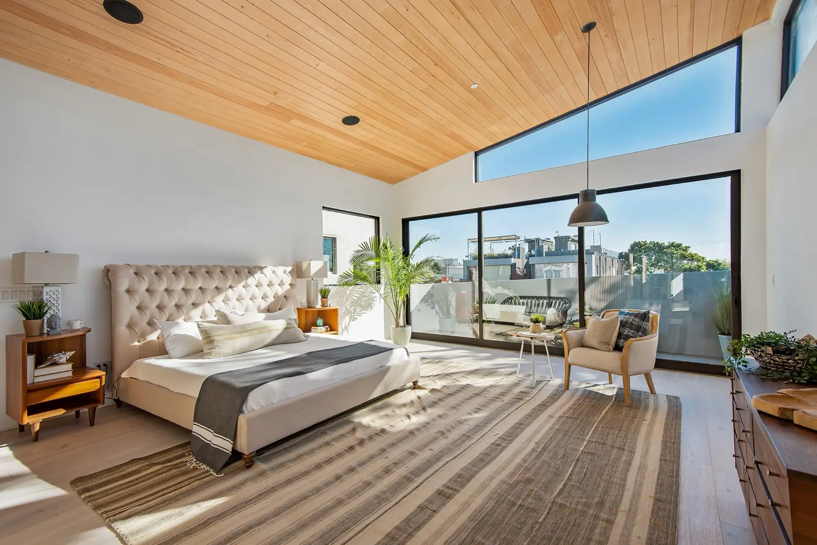 A finished Farnsworth Builders interior — a bedroom with a vaulted timber ceiling and full-height glazing opening onto a terrace.