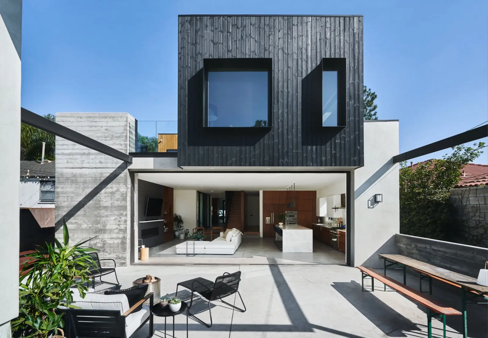A completed Farnsworth Builders home — a dark timber-clad upper volume cantilevered over an open living space that folds out to a concrete terrace.